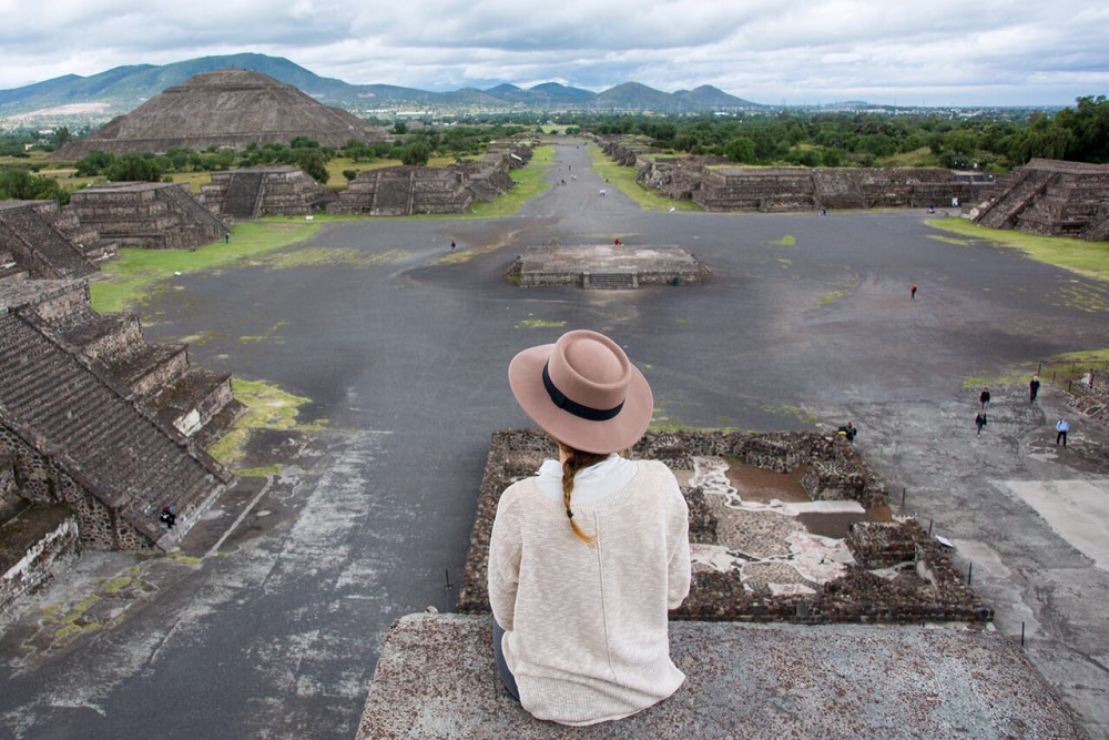 A woman sitting on top of a pyramid in Teotihuacan, overlooking the site and other structures