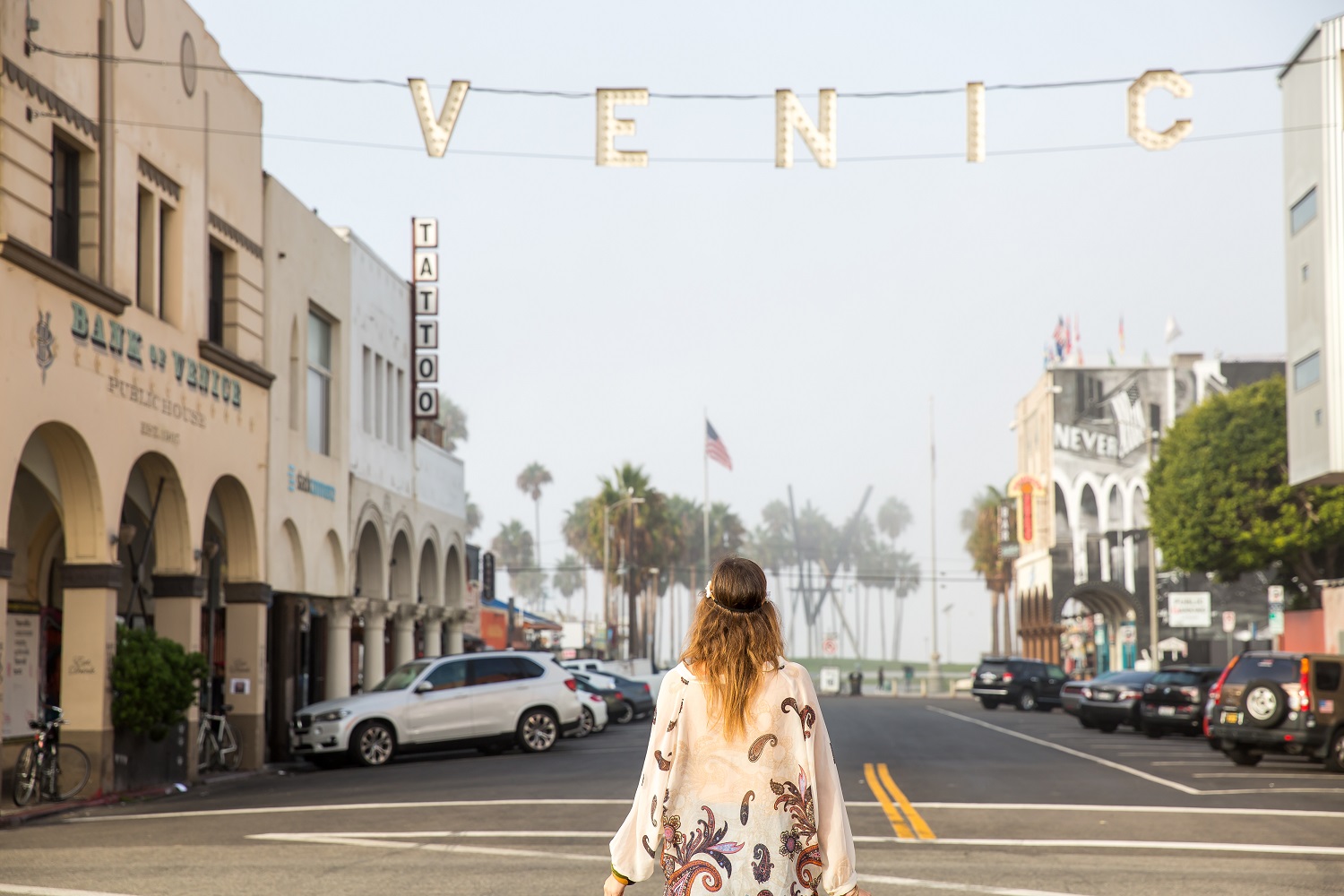 A woman standing in the street in Venice Beach, under a sign that reads ''Venice''