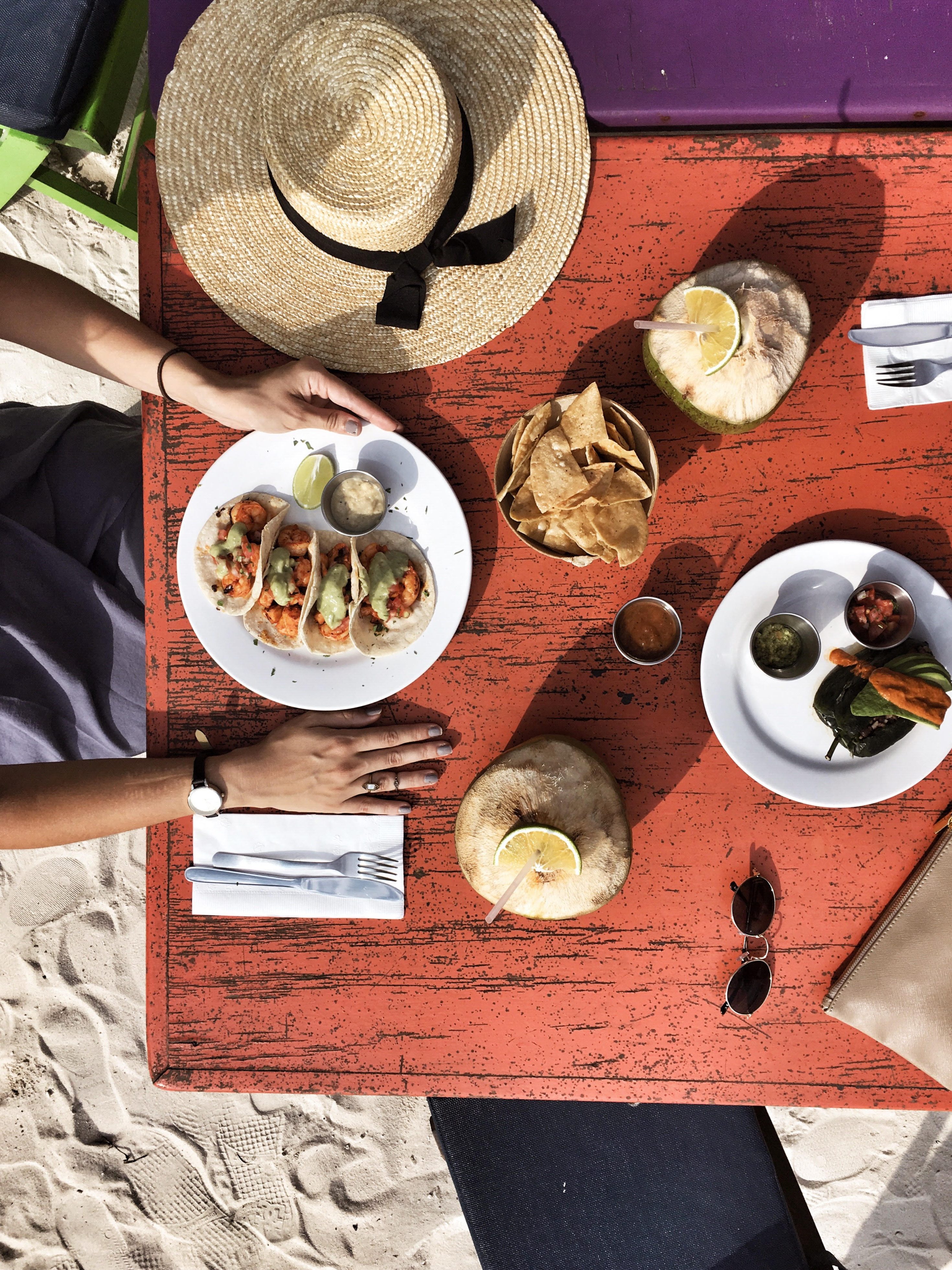 A breakfast table on the beach, with a plate of tacos, a bow of chips, and two coconuts inserted in a post about the perfect day trip to Tulum from Cancun
