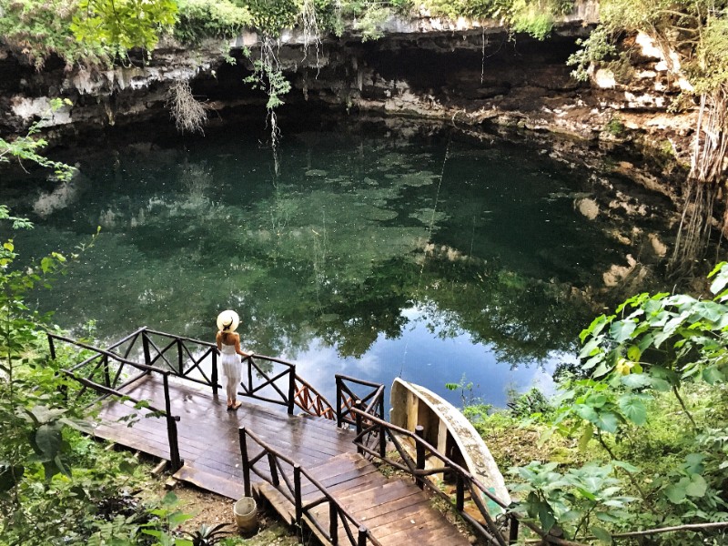 Woman with a white dress standing in front of an open cenote, inserted in a post about the best cenote tours from Valladolid.