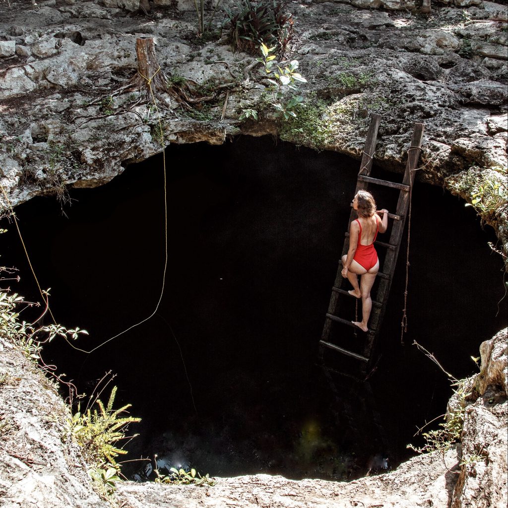 Woman on the ladder descending into Cenote Calavera, Mexico.