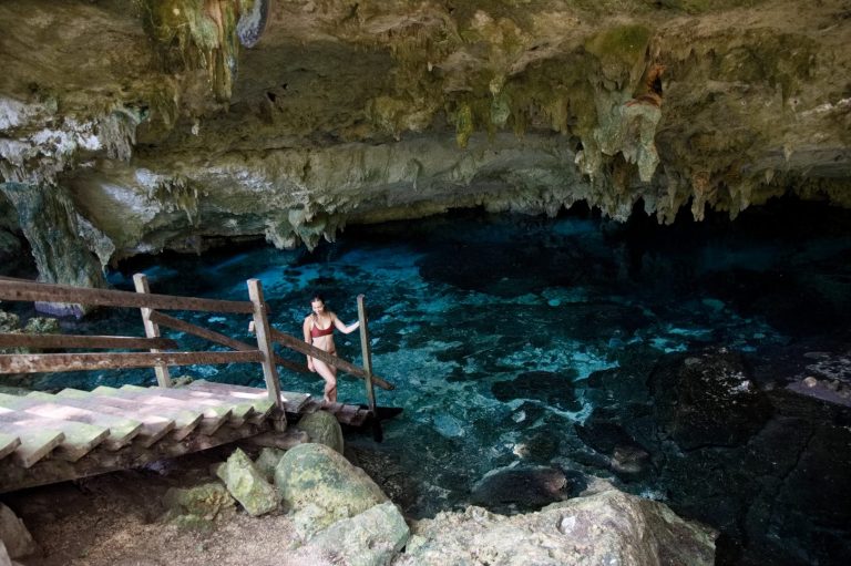 A woman at the bottom of a wooden staircase beside the water in the Dos Ojos cave.
