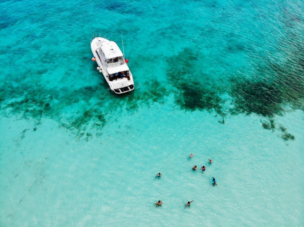 A drone image of the turquoise Caribbean Sea, a white yacht, and people swimming, inserted in a post about Cancun Catamaran cruises