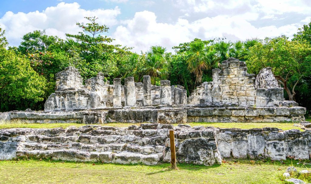 A very colorful image of El Rey, one of the best Mayan ruins in Riviera Maya. The ruins of an ancient building are surrounded by green vegetation