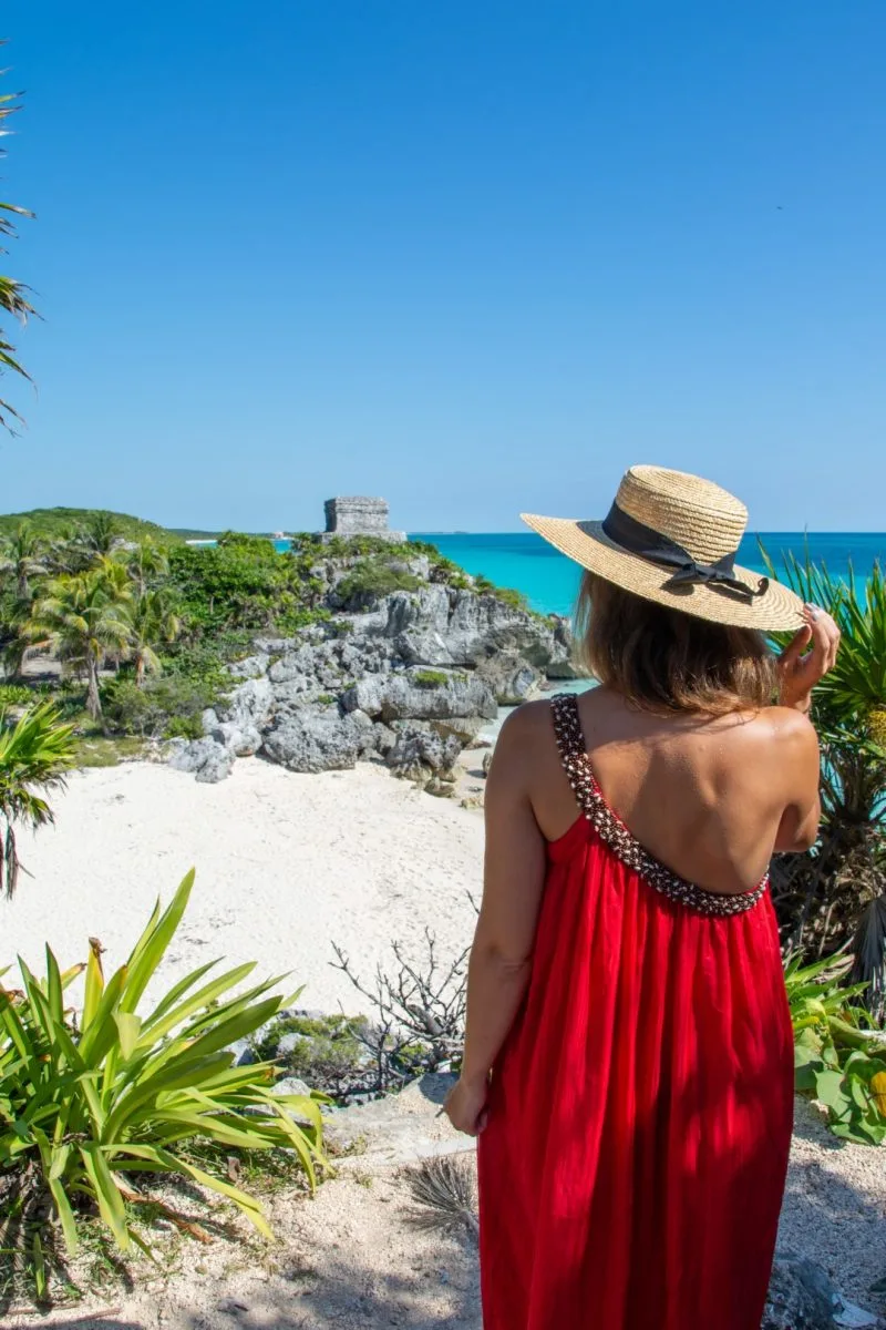 Woman with red dress standing in front of the Castillo at the Tulum Ruins.