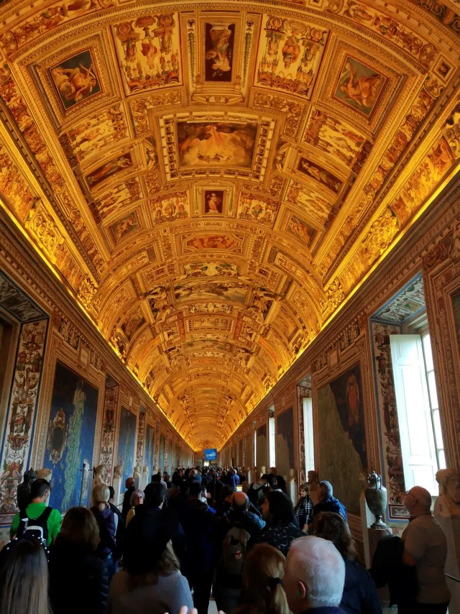 A corridor in the Vatican museums, with an arched and frescoed ceiling, and a great number of people walking