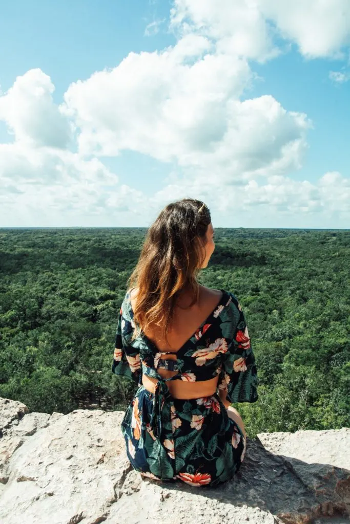 A woman sitting on top of a Mayan pyramid in Coba, admiring the lush vegetation around it 