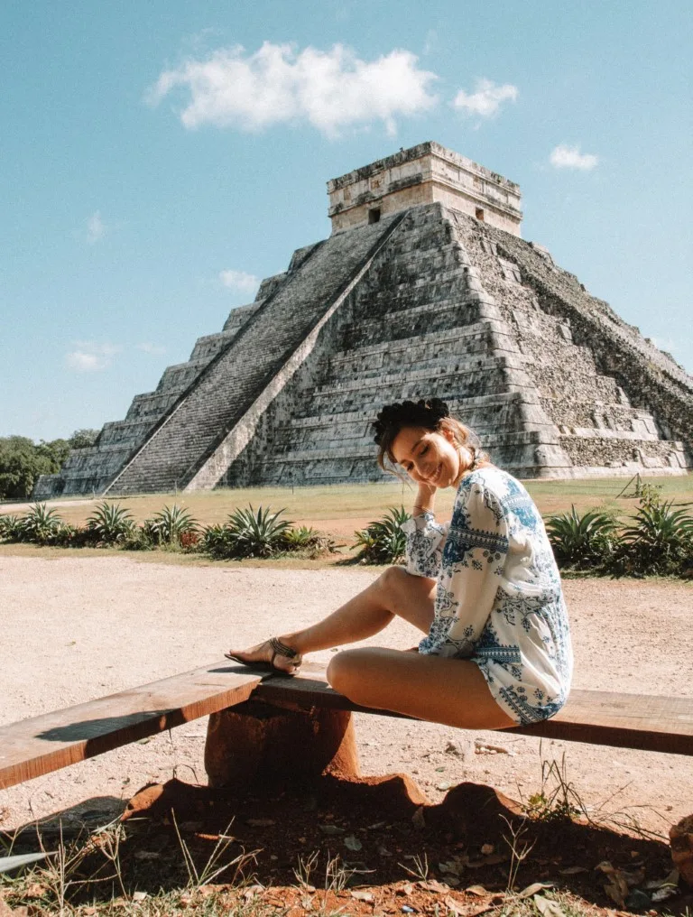 A woman sitting on a bench in front of Chichen Itza's main pyramid, inserted in a post about Mayan ruins. 