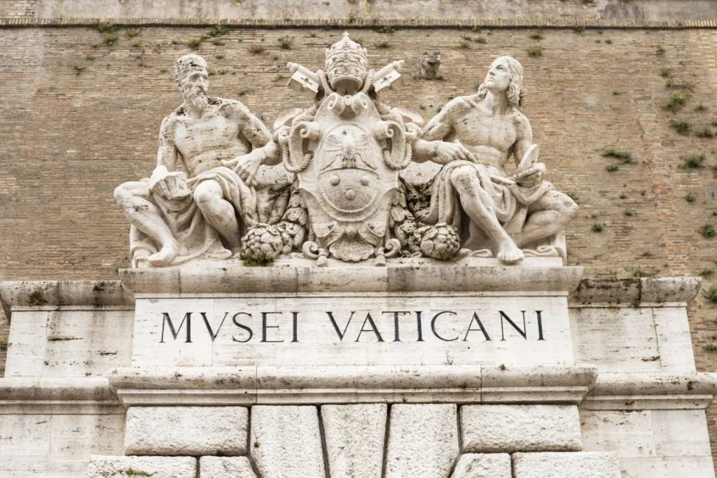 A sculpture of two men and a coat of arms at the entrance of the Vatican Museums 