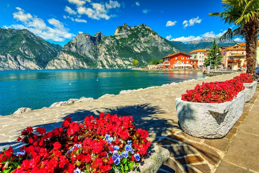Lake Garda, with mountains in the background, and red flower pots on the side of the lake