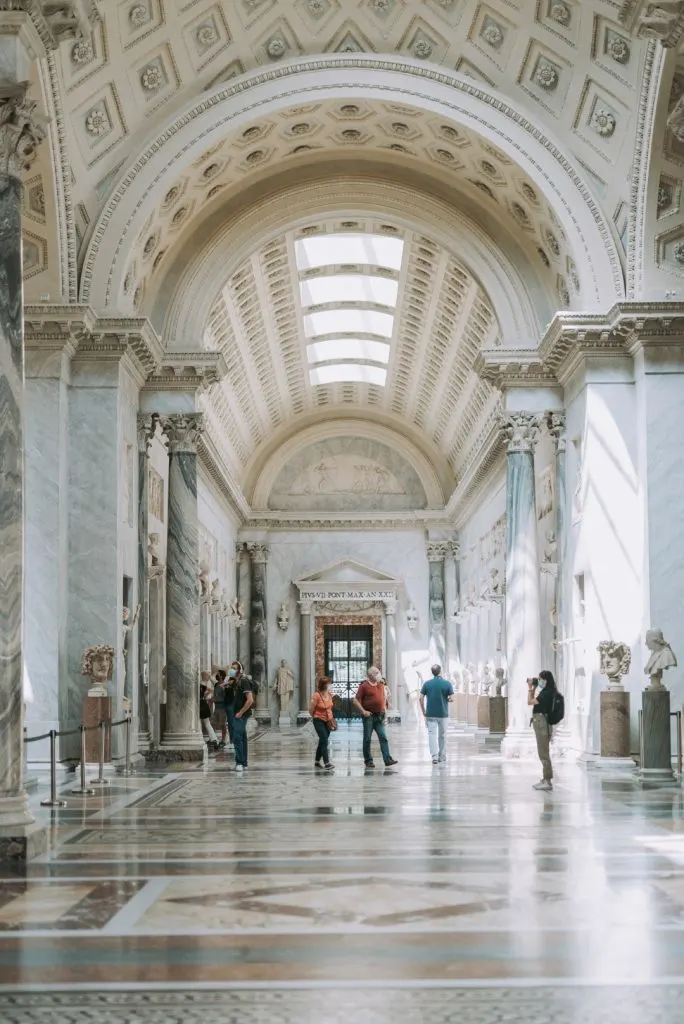 Inside the Vatican Museums, a corridor with white walls, marble columns, and an arched ceiling. Image inserted in a post about Sistine Chapel tickets 