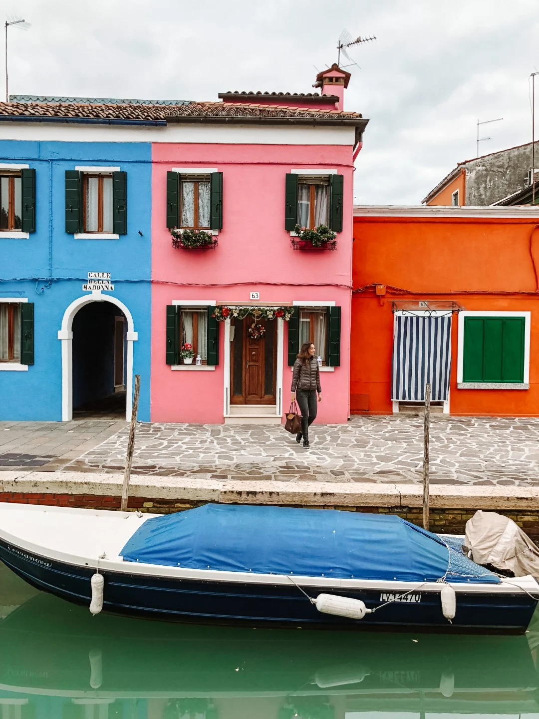 A woman standing in front of three colorful houses, a blue, a pink, and an orange one