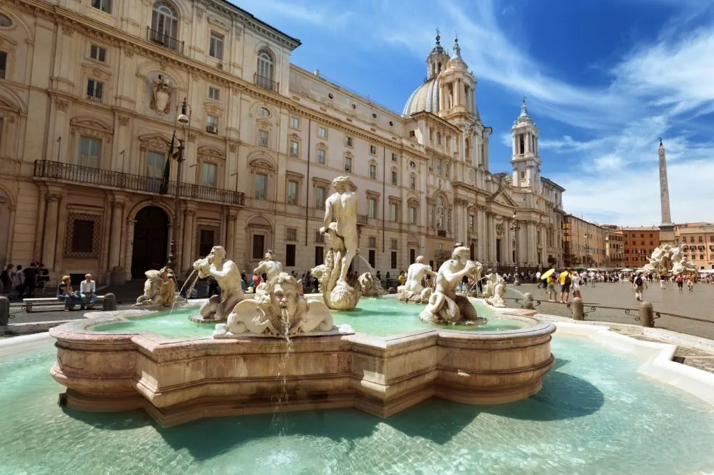 A fountains with sculptures in Piazza Navona, with an elegant building in the back
