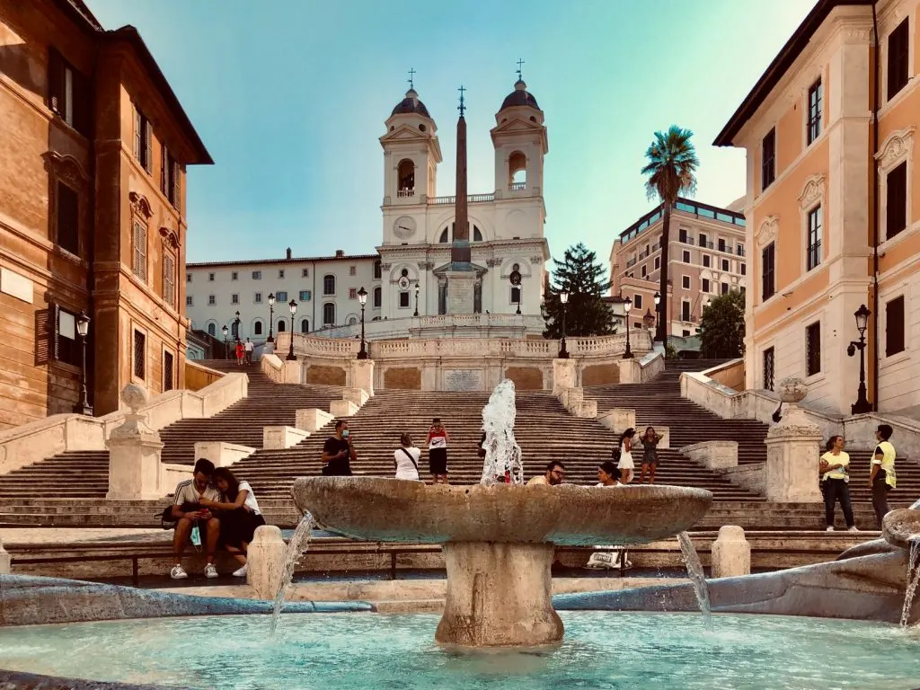 A water fountains in Piazza Spagna, with the Spanish Steps in the background