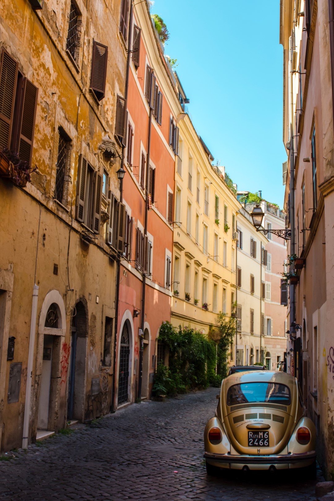 A cobblestone street lined with pastel-colored buildings, and with a beetle car parked on the side. Image inserted in a post about a day trip from Florence to Rome