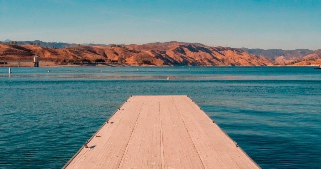 A wooden pier surrounded by the water of Castaic Lake, with reddish mountains in the distance 