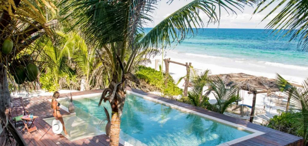 A woman standing on the edge of a pool, surrounded by palm trees and overlooking the sea