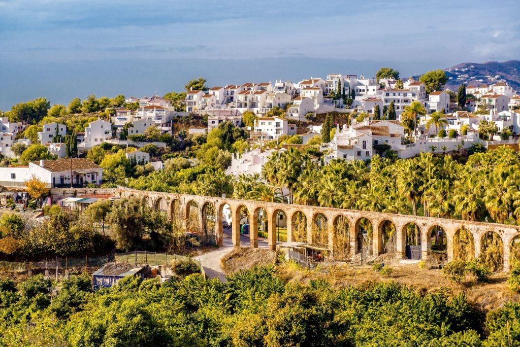Image of an aqueduct surrounded by palm trees and with white houses dotted in the background. It's an image of  Queretaro, one of the Unesco World Heritage Sites in Mexico