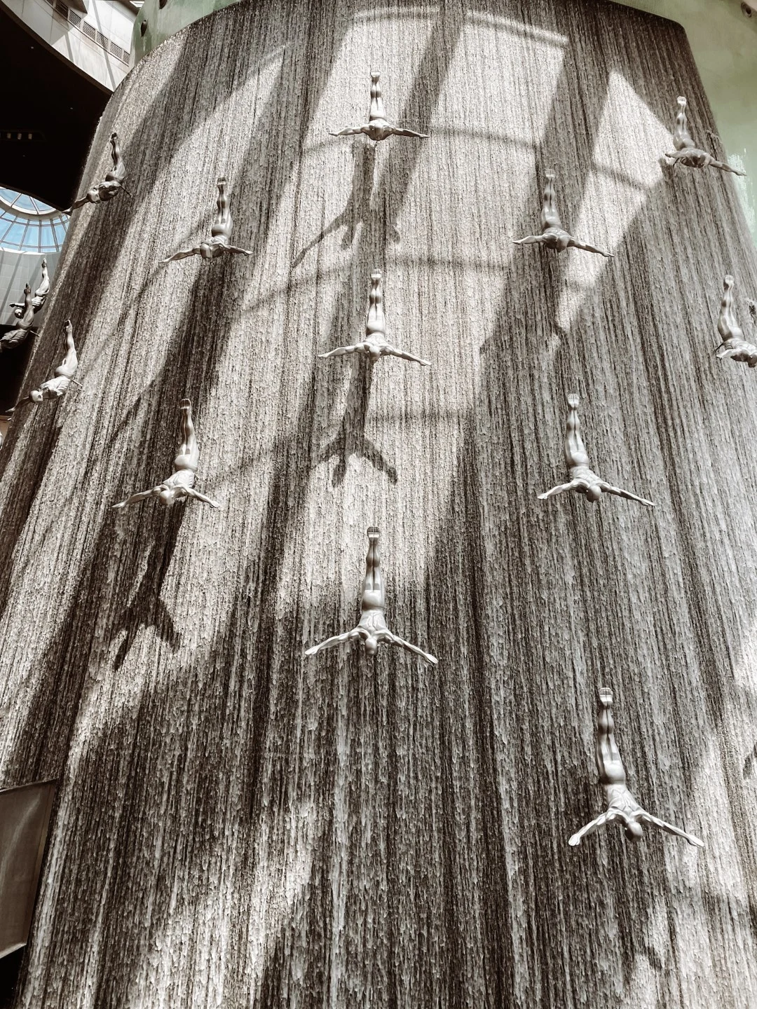 An image of Dubai Mall Fountain, with sculptures of men diving down. Checking it out is one of the best things to do at Dubai Mall.  