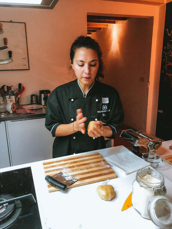 Chef in a black uniform rolling fresh pasta dough by hand on a kitchen counter.