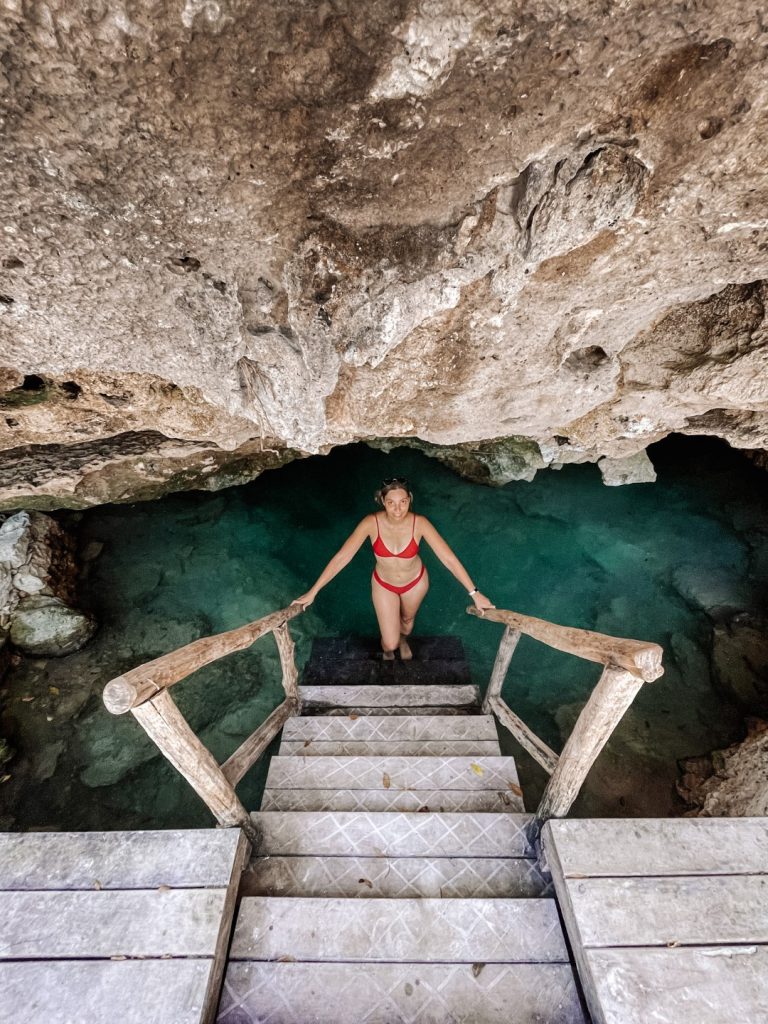 Woman at the bottom of a ladder that leads into a cenote, with a limestone wall behind her. Image inserted in a port about the perfect Tulum itinerary