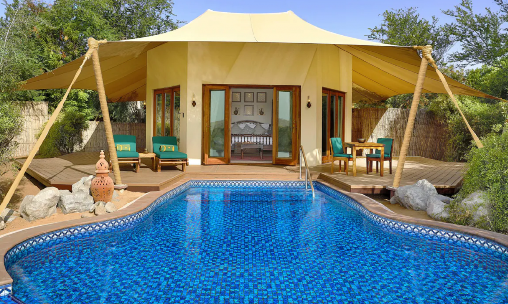 A luxurious yellow tent surrounded by a wooden deck with sun loungers, and a large swimming pool. It's a room in Al Maha, one of the best hotels with private pools in Dubai 