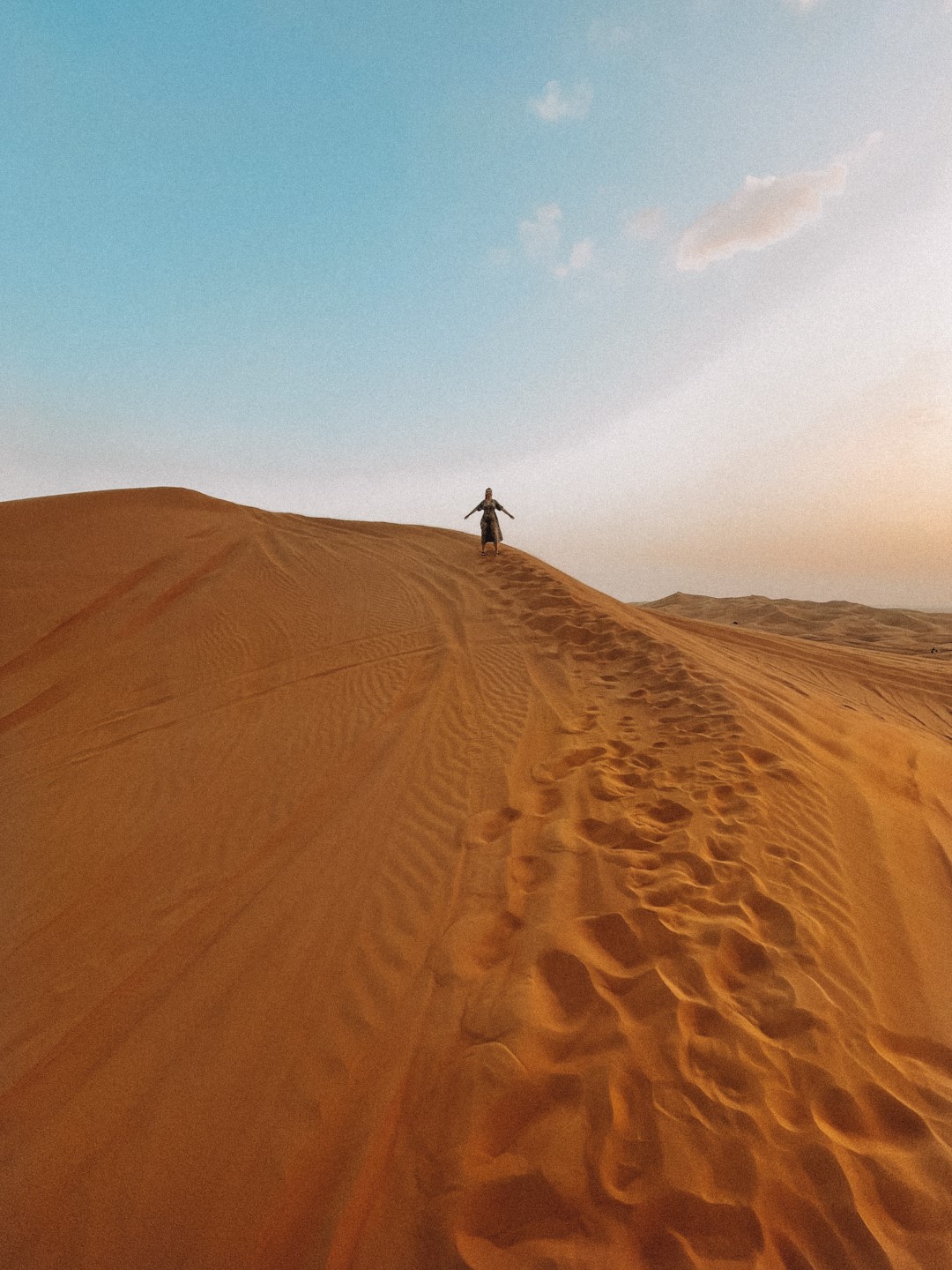 Image of a woman on a dune in the desert in Dubai, inserted in a post about the best Dubai desert safari to book.