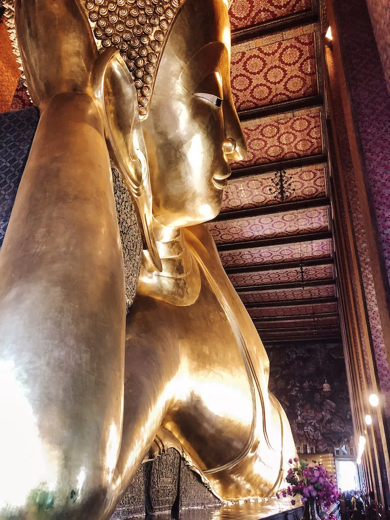 Image of a giant golden Buddha in a reclining position pictured from below, inserted in a post about the best temples in Bangkok