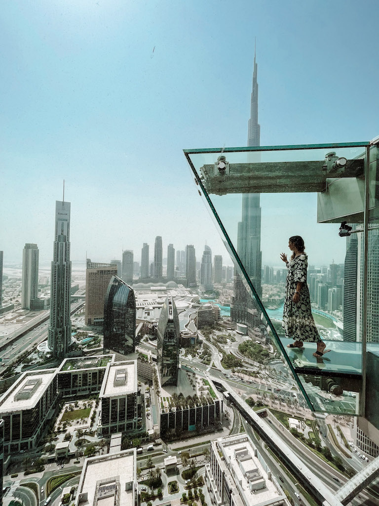 Woman standing on a platform at Sky Views Dubai with Burj Khalifa in the background.