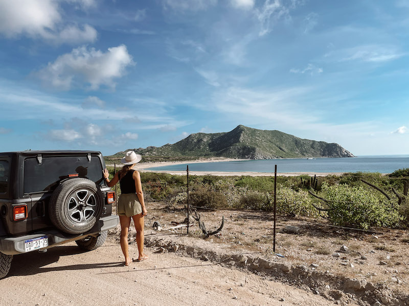 A woman standing next to a jeep, and looking at the bay in Cabo Pulmo Park 