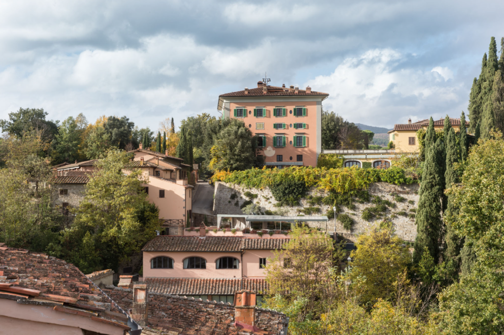 Image of Il Borro hotel seen from afar, surrounded by trees and other pastel-colored houses