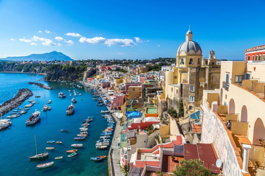 Image of a coastline, with very colorful houses on the right and the blue sea on the left, dotted with fishing boats. Picture inserted in a post about things to do in Naples