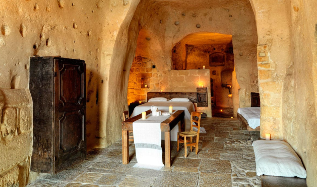 A cave hotel room in Matera, equipped with a wooden table and wardrobe, a bed, and candles