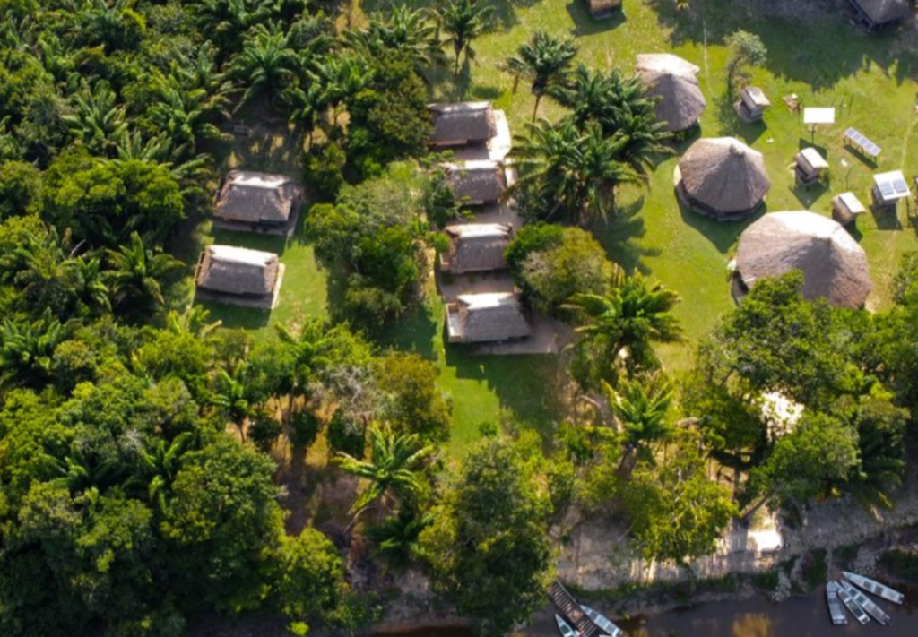 Image of an ecolodge in Guyana seen from above, with green vegetation and thatched roofs scattered around
