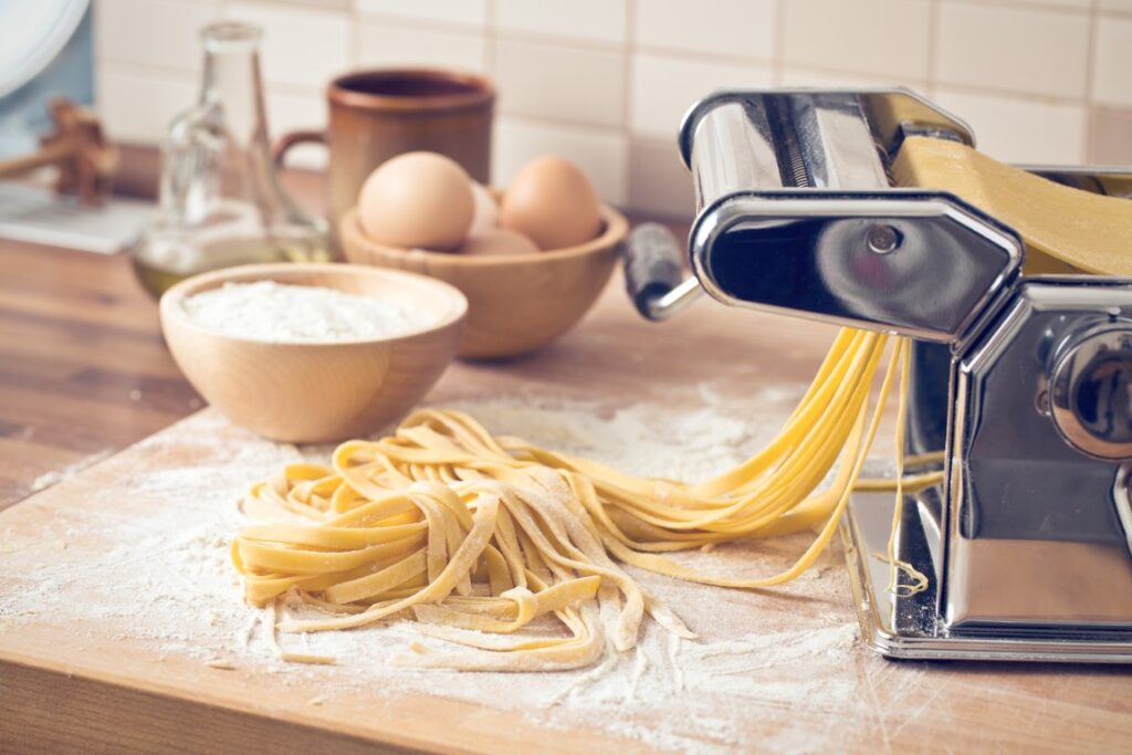 Image of fresh pasta and a pasta machine on a wooden table, inserted in a post about the best cooking classes in Lake Como.