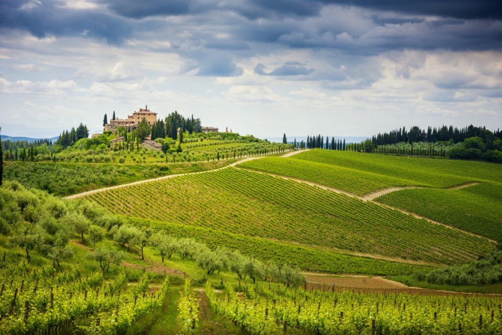 Image of the Chianti hills with rolling vineyards, cypress trees and an old Tuscan villa in the background, inserted in a post about Rome to Tuscany Day Trips & Tours.