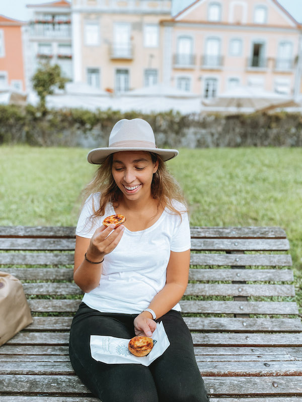 Woman sitting on a bench eating a pastel de nata during one of the best food tours in Lisbon.