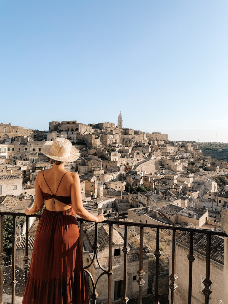 Woman from the back with a dress and hat looking at Sasso Caveoso in Matera.