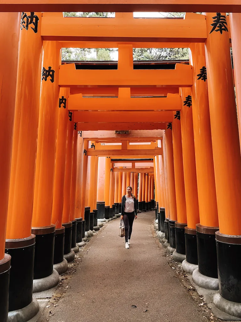 A woman walking under vermilion torii gates