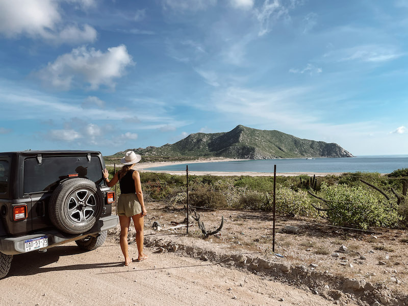 Woman standing by a Jeep and looking at the Cabo Pulmo coastline 