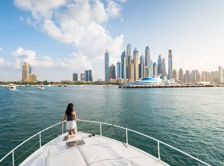 Woman kneeling at the bow of a yacht looking at the skyline of Dubai Marina during a Dubai Marina cruise.