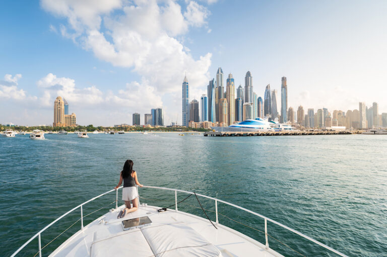 Woman kneeling at the bow of a yacht looking at the skyline of Dubai Marina during a Dubai Marina cruise.
