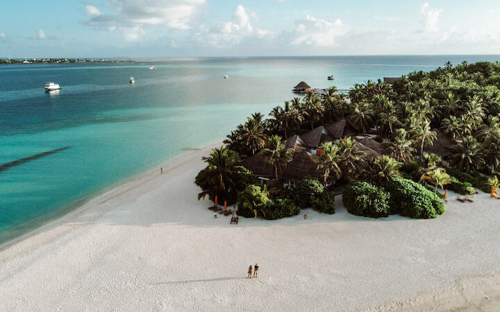 Drone photo of two people standing on the beach at Angsana Velavaru, one of the best eco resorts in the Maldives.