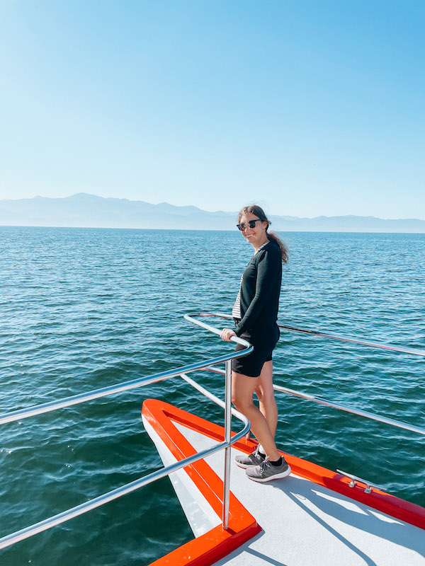 Woman standing at the edge of a boat and smiling at the camera during a Puerto Vallarta whale watching tour.