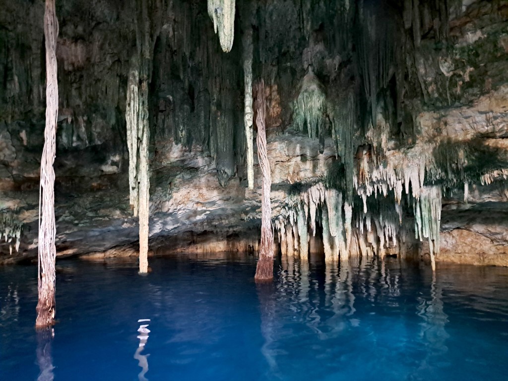 A cave cenote with stalactites and blue water, inserted in a post about Coba Ruins, Mexico: A Complete Guide