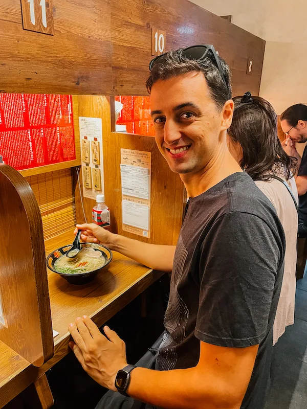 A man sitting at a small table with a bowl of ramen in front of him