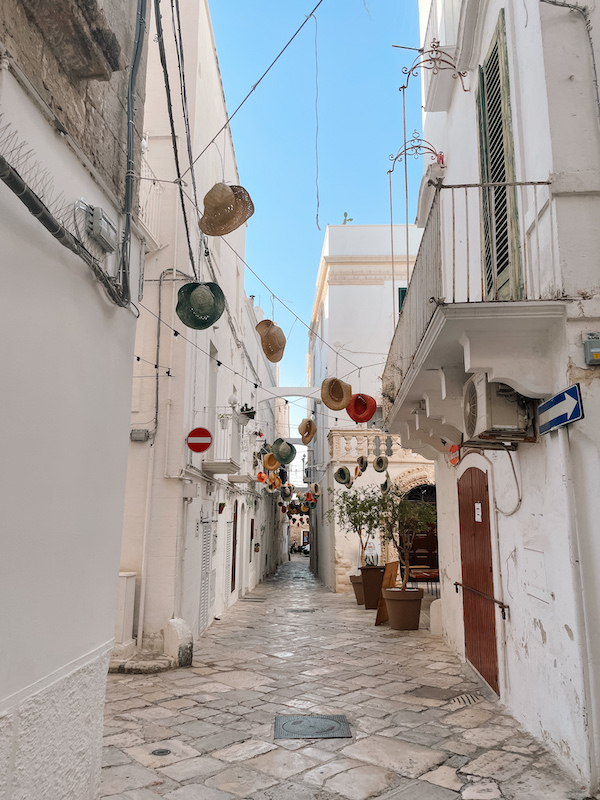 A narrow alley lined by white buldings, and hats hanging over it