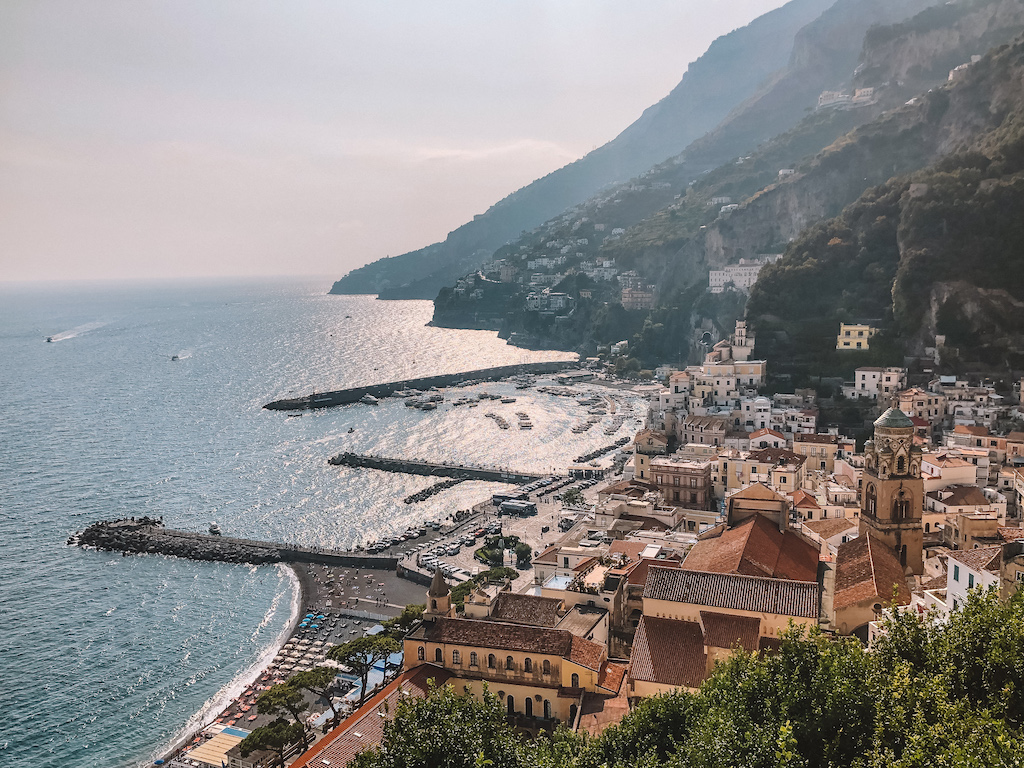 Scenic view of the Amalfi Coast with its pastel-colored buildings, a picturesque harbor, and dramatic cliffs meeting the sparkling Mediterranean Sea.