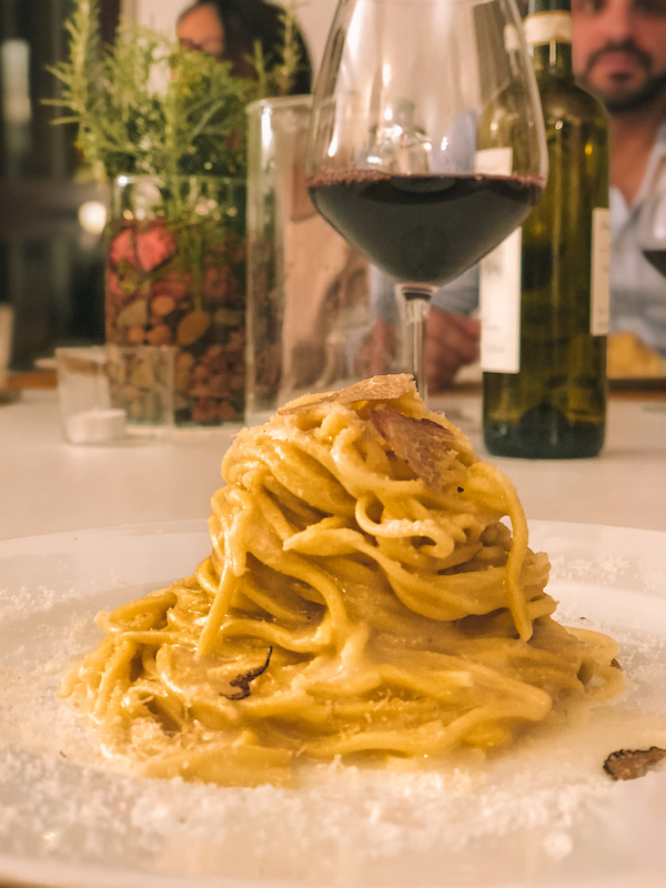 Plate of fresh pasta with creamy sauce and truffle shavings, served with a glass of red wine on the table.