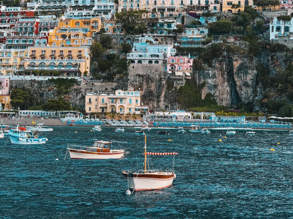 Multiple boats in the sea in Positano with the cliff and colorful houses in the background.